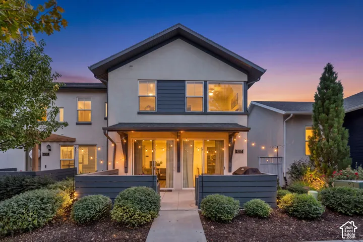 Two-story stucco exterior featuring horizontal siding accents, a paved ground-level patio, private horizontal slat fencing, and large windows
