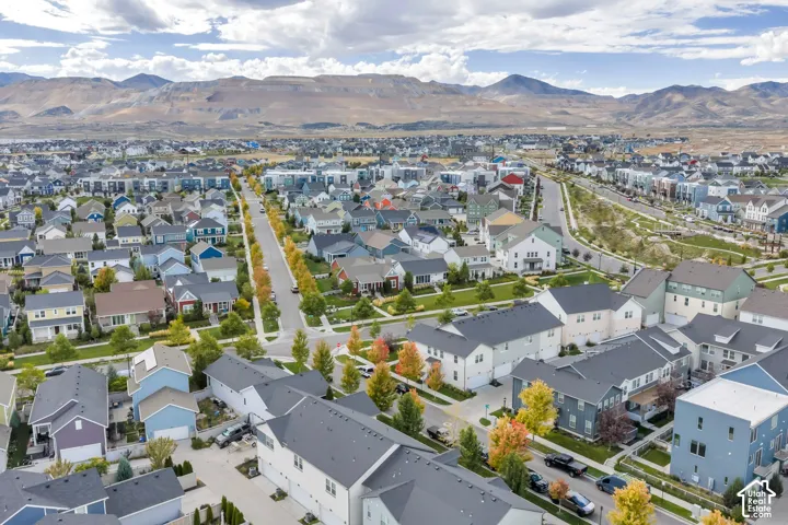Aerial perspective of a suburban neighborhood featuring a grid of residential homes, tree-lined streets, and a prominent mountain range backdrop
