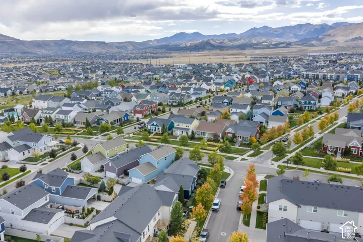 Aerial perspective of a suburban neighborhood featuring a grid of residential properties, paved streets, mature deciduous trees, and a mountain range backdrop