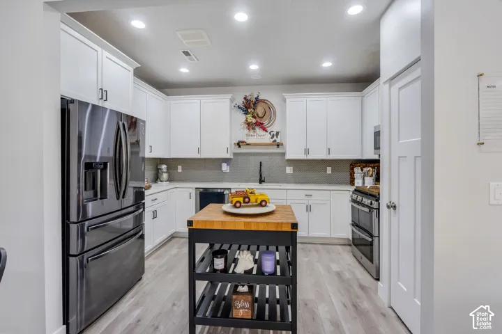 Kitchen featuring white shaker-style cabinetry, stainless steel appliances, wood-finish flooring, recessed lighting, and solid-surface countertops