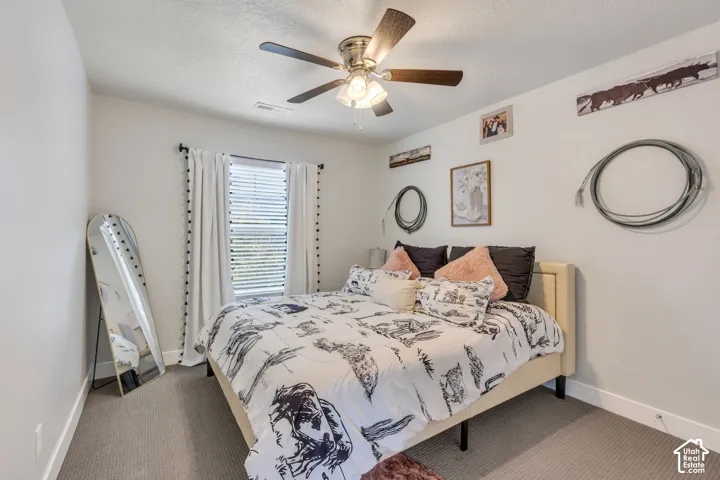 Bedroom featuring neutral wall paint, gray wall-to-wall carpeting, window with slatted blinds, and a multi-blade ceiling fan with an integrated light fixture