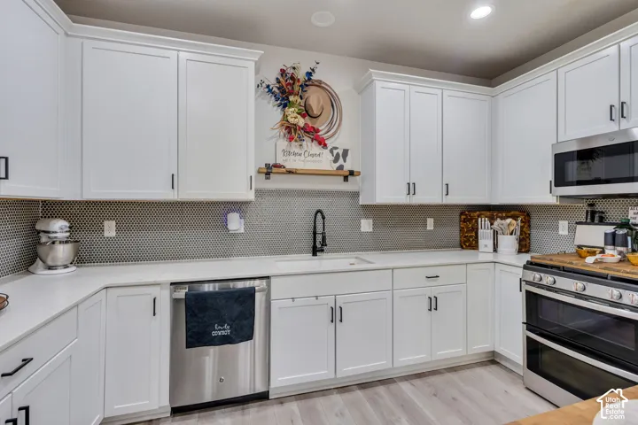 Kitchen featuring white shaker-style cabinetry, matte black hardware, stone-composite countertops, penny-round mosaic tile backsplash, and stainless steel appliances