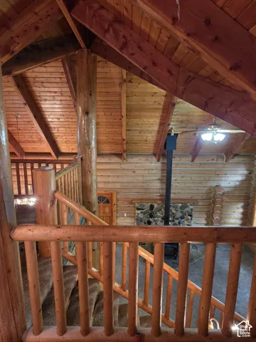 Vaulted ceilings with exposed timber beams, log walls, log-post railing, floor-to-ceiling stone fireplace surround, and wood-finish ceiling paneling
