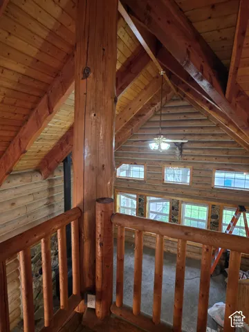 Vaulted wood-paneled ceiling with exposed timber beams, full-log wall construction, and custom log railings