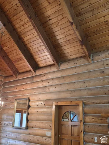 Log wall construction featuring exposed timber beams, vaulted tongue-and-groove wood ceiling, and a paneled wood door with an arched glass insert