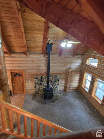 Exposed timber vaulted ceiling, full-log walls, floor-to-ceiling stone hearth, freestanding wood-burning stove, and natural wood railings