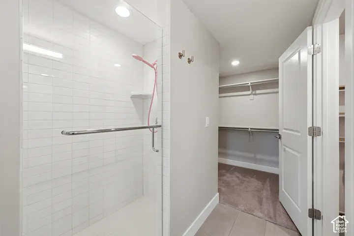 Walk-in shower with white tile surround, glass enclosure, and handheld sprayer, featuring tile flooring and built-in closet with shelving