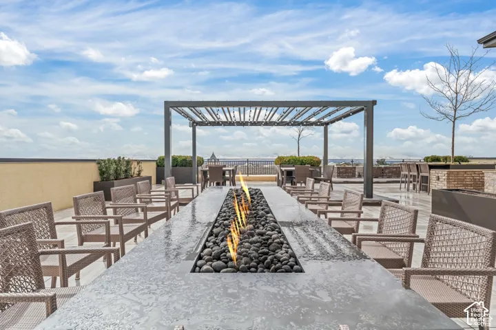 Rooftop terrace featuring a linear stone-surround fire pit, metal-frame pergola, stone tile flooring, and integrated stone-faced bar area