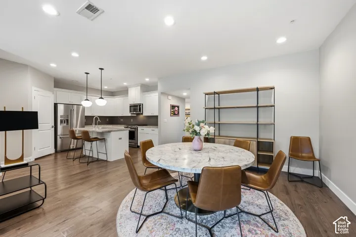 Kitchen featuring white shaker-style cabinetry, stainless steel appliances, a central island with a stone countertop, recessed lighting, and wood-finish flooring