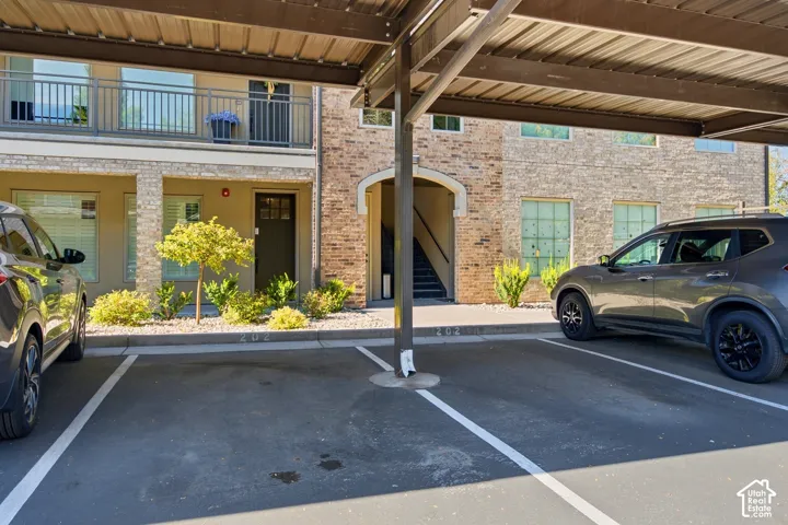 Covered parking stall featuring a brick exterior facade, arched entryway, and metal balcony railing