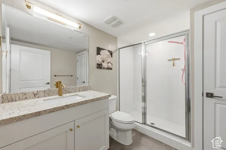 Bathroom featuring a white shaker-style vanity with stone-finish countertop, undermount sink with gold-tone faucet, large wall-to-wall vanity mirror, and a walk-in shower with tiled walls and glass enclosure