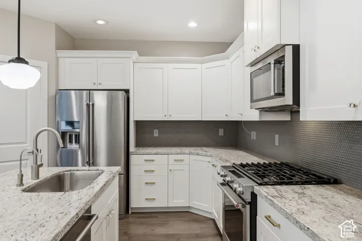 Kitchen featuring white cabinetry, light stone countertops, stainless steel appliances, a honeycomb-patterned backsplash, and a pendant light fixture