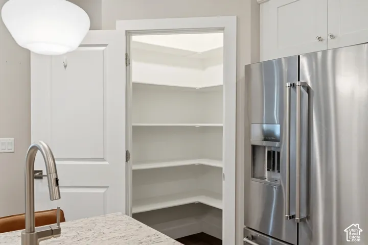 Walk-in pantry with white built-in shelving, stainless steel refrigerator, stone-finish countertop, and stainless steel gooseneck faucet