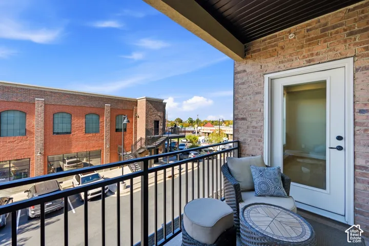 Covered exterior balcony featuring a brick facade, black metal railing, and a glass-paneled entry door