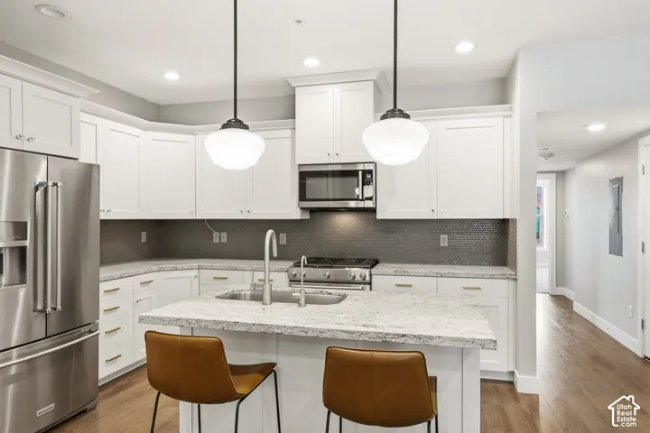 Kitchen featuring white cabinetry, stone countertops, stainless steel appliances, a tile backsplash, and pendant lighting over an island