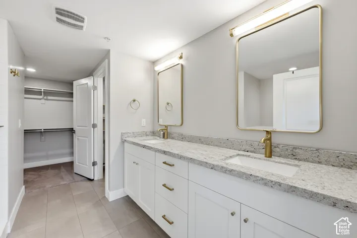 Double vanity featuring white cabinetry, stone-style countertops, integrated dual sinks, gold-tone fixtures, and rectangular mirrors