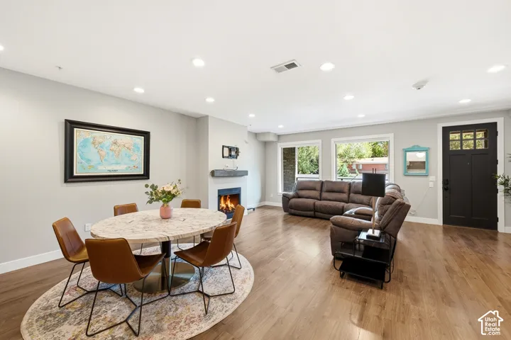Open-concept interior featuring wood-finish flooring, recessed lighting, a fireplace with a decorative mantel, and a multi-panel front door with glass insets