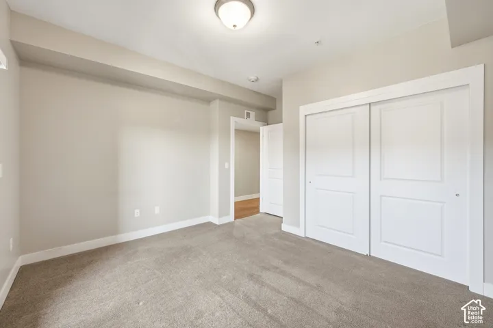 Neutral-toned interior space featuring carpeted flooring, sliding-panel closet doors, and overhead flush-mount lighting