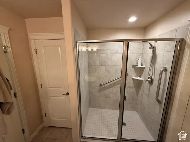 Walk-in shower featuring tile walls, a handheld showerhead, two built-in corner shelves, and two grab bars enclosed by a glass door