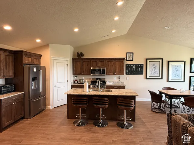 Kitchen featuring wood-finish flooring, vaulted ceilings, recessed lighting, stone-surface countertops, and dark-toned built-in cabinetry
