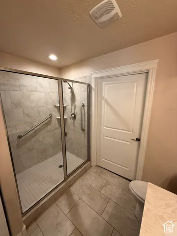 Walk-in shower with metal-framed glass enclosure, tiled wall surround, integrated shelving, and stainless steel grab bars, complemented by neutral tile flooring