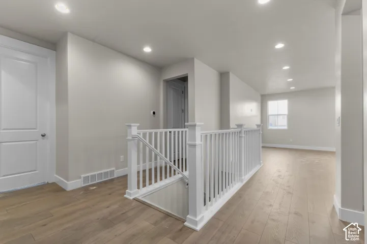 Neutral wall tones, wood-finish flooring, recessed lighting, and white wooden stair railing