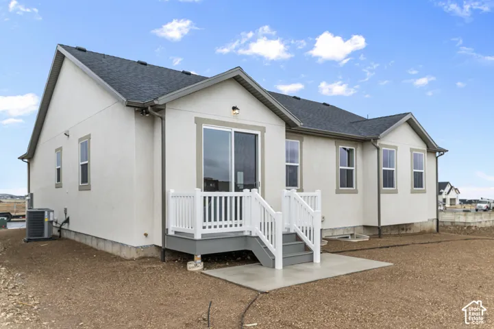Stucco exterior featuring a dual-gabled roofline, sliding glass door, white railing, and a concrete patio