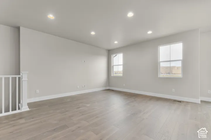 Neutral interior space featuring wood-finish flooring, recessed lighting, dual-pane windows with muntins, and a white balustrade
