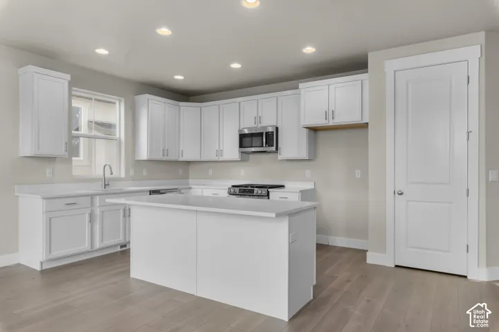 Kitchen featuring white shaker-style cabinetry, quartz countertops, a central island, recessed lighting, and wood-finish flooring