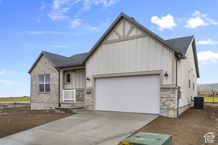 Single-story residence featuring a mixed-material facade of stone veneer and vertical siding, gable roofline, attached two-car garage, and concrete driveway