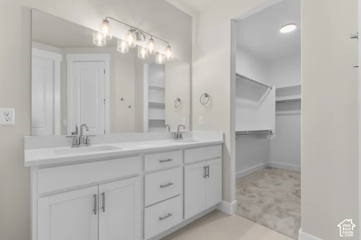 Double vanity featuring white shaker-style cabinetry, solid-surface countertops, dual integrated sinks, and a large-format vanity mirror with integrated multi-bulb lighting