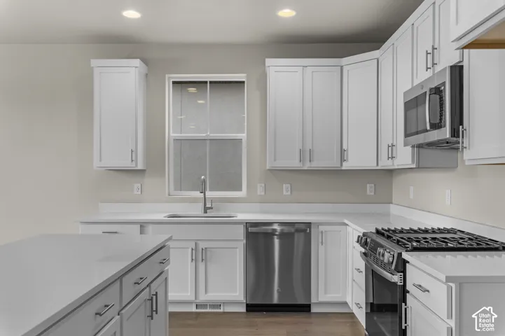 Kitchen featuring white shaker-style cabinetry, solid-surface countertops, stainless steel appliances, recessed ceiling lighting, and wood-finish flooring