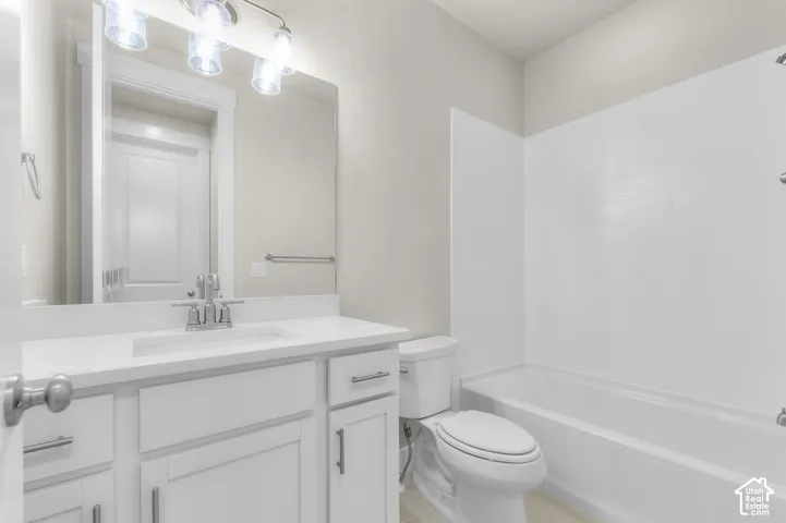 Bathroom featuring a white vanity cabinet, rectangular under-mount sink, white countertop, three-light fixture, and a white tub-shower combination
