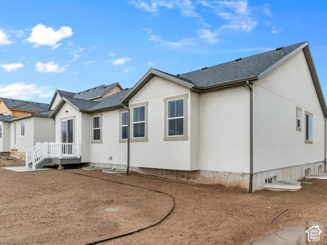 Stucco exterior featuring an asphalt shingle roof, multi-gabled roofline, grid-pattern windows, and a raised composite deck with white railings