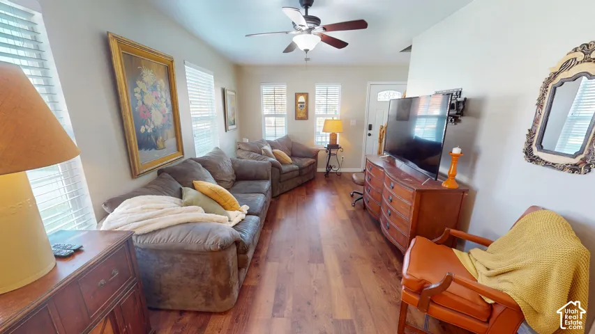 Living space featuring wood-finish flooring, ceiling fan with light fixture, and multiple windows with horizontal blinds
