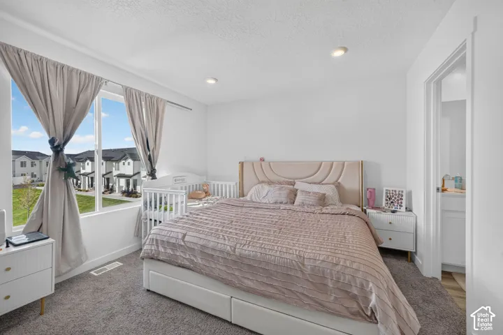 Carpeted bedroom featuring recessed lighting, a large window, and an adjacent bathroom
