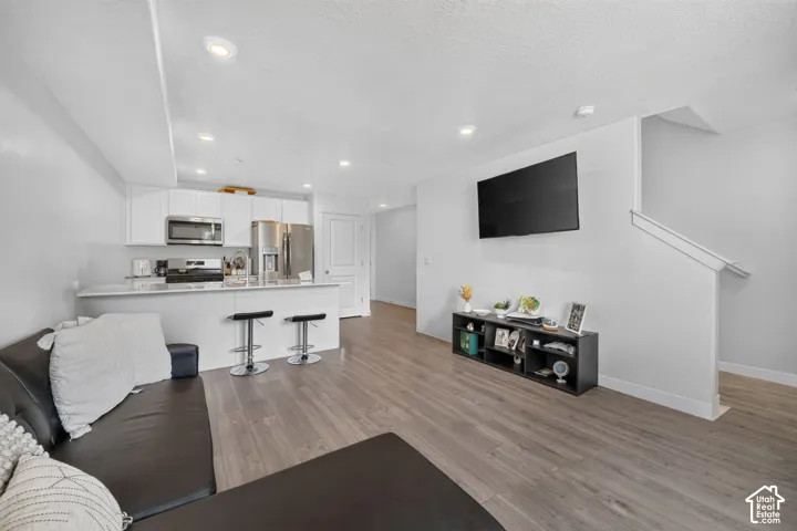 Open-concept living area with wood-finish flooring, recessed lighting, and a white kitchen featuring stainless steel appliances