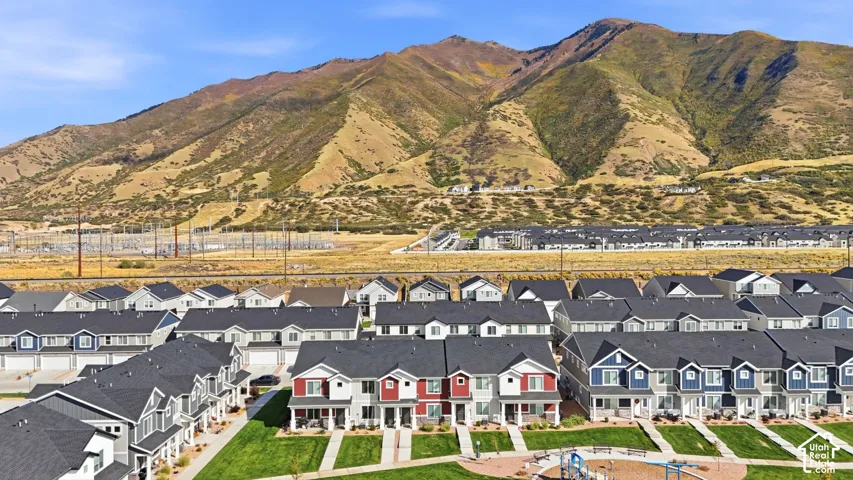 Community of townhomes with varied exterior finishes and mountain backdrop, featuring paved pathways and green spaces
