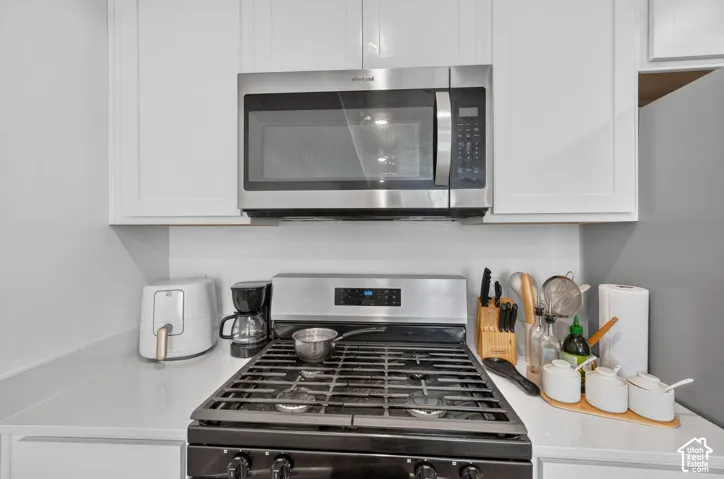 White shaker-style cabinetry, stainless steel microwave, black gas range, and white countertops