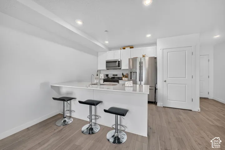 Kitchen featuring a breakfast bar with seating, stainless steel appliances, white cabinetry, and wood-finish flooring