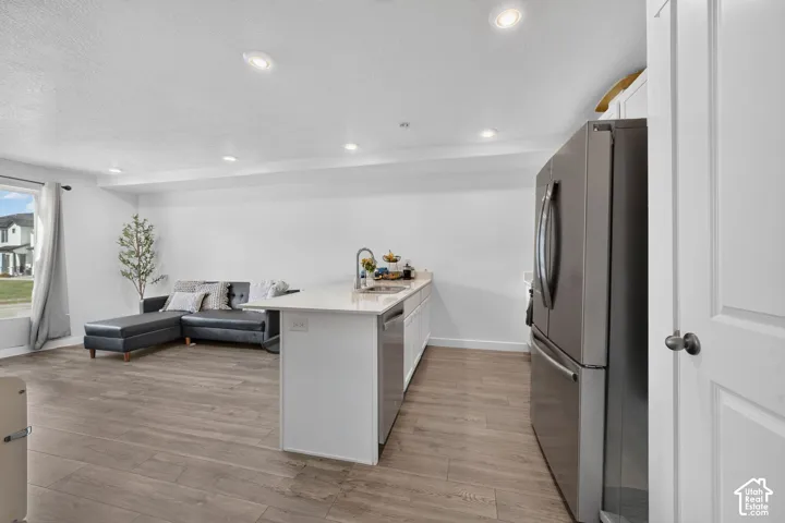 Open-concept living area with wood-finish flooring, recessed lighting, and a kitchen island featuring a sink and white countertop