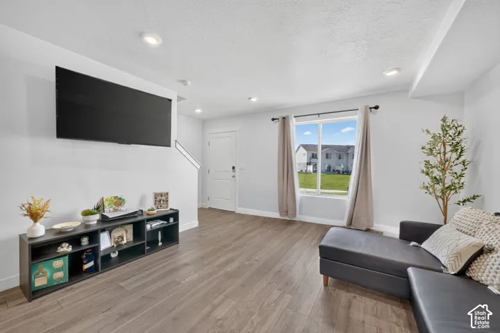 Expansive room with wood-finish flooring, recessed lighting, a large window, and a white entry door