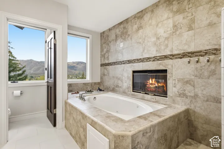 Built-in soaking tub, tiled surround, integrated fireplace, and multiple windows