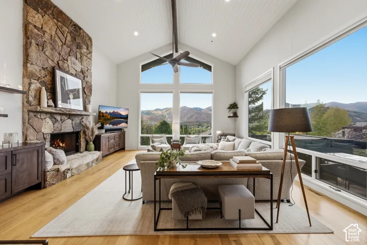 Vaulted ceiling with wood-finish planks, stacked stone fireplace with hearth, and large windows providing expansive mountain scenery