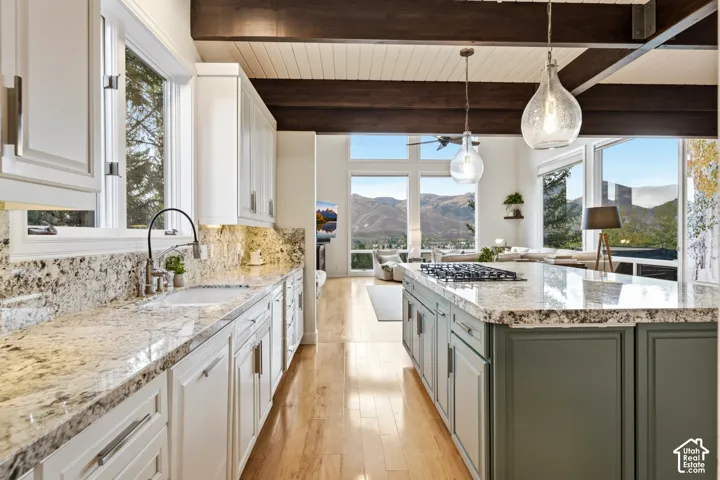 Gourmet kitchen featuring a large island with cooktop, granite countertops, wood-finish flooring, custom cabinetry, and expansive windows
