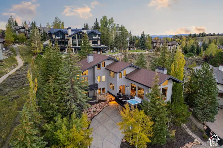 Multi-level residence featuring a brown shingle roof, light gray siding, multiple large windows, a deck with an outdoor spa, and a paved driveway