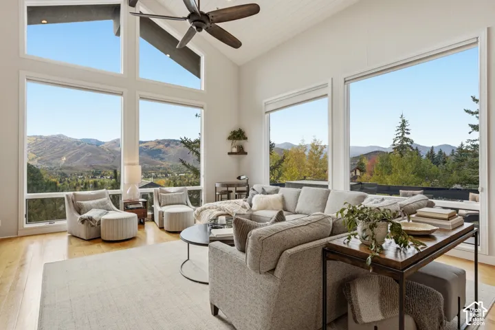 Vaulted ceiling with wood-finish fan, expansive windows, light wood-finish flooring, and mountain scenery