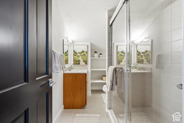 Sliding glass shower enclosure with tiled walls, vanity with a light wood-finish cabinet, granite-style countertop, and integrated sink