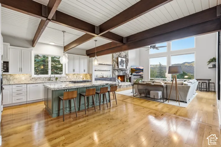 Open-concept living area with wood-finish flooring, exposed beam ceiling, stone fireplace, and a kitchen island with seating