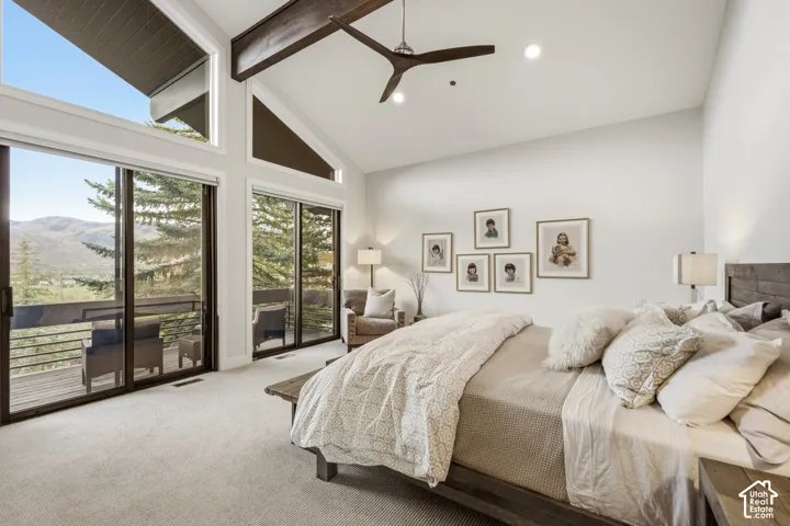 Vaulted ceiling with exposed wood beams, wall of windows, sliding glass doors to outdoor balcony, light neutral carpeting, and recessed lighting